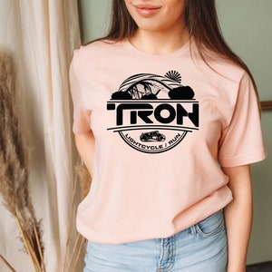 May include: A pink t-shirt with a black circle graphic featuring the word "TRON" and the text "LIGHTCYCLE / RUN".