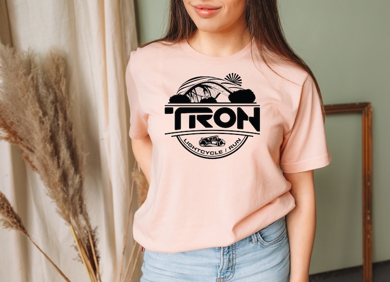 May include: A pink t-shirt with a black circle graphic featuring the word "TRON" and the text "LIGHTCYCLE / RUN".