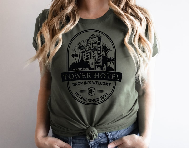 May include: A green t-shirt featuring a black graphic of the Hollywood Tower Hotel. The graphic includes the text "The Hollywood Tower Hotel", "Drop In's Welcome", and "Established 1994".