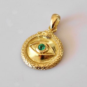 May include: Gold pendant necklace featuring a round eye with a green gemstone set in the center, surrounded by a snake design.