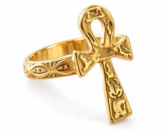 May include: A gold-toned ring featuring an ankh symbol as the centerpiece. The band is decorated with a repeating eye-like pattern, while the ankh is engraved with various small, intricate symbols across its surface.