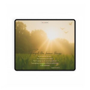 May include: A rectangular mousepad featuring a serene landscape with a bright sun, trees, and grass. The text "Forget the former things" is written in elegant script, along with a Bible verse. The color palette includes greens, yellows, and browns.