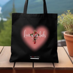May include: Black tote bag with a pink heart design featuring a cross with red roses and the text "Love never fails 1 Corinthians 13:8" and the text "The 13:1 Letter Words."