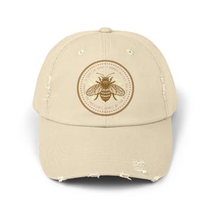 May include: A beige distressed baseball cap with a brown and yellow bee graphic and the text "If God can make a bumble bee fly, don't you think He can do the impossible?"