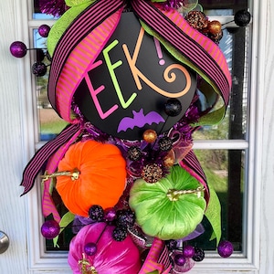 May include: A Halloween door wreath with a black sign that says "EEK!" with a bat, green, pink, and black striped ribbon, and velvet pumpkins in orange, green, and pink.