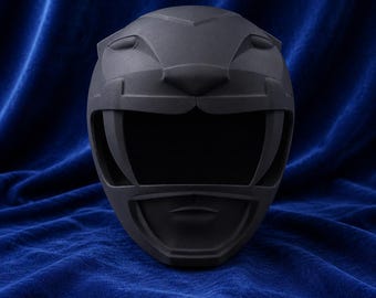 May include: A matte black full-face helmet featuring a stylized feline design with sculpted ears, a prominent nose bridge, and large eye openings. The helmet has a smooth, uniform finish and a wide, dark visor area that covers the upper face section.