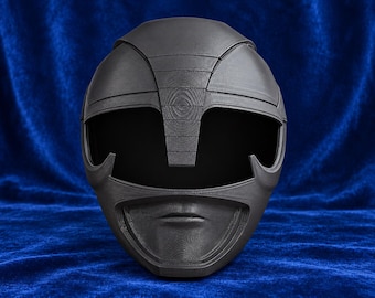 May include: A matte black full-face helmet featuring a distinct visor opening and a molded mouth guard section. The surface displays a visible layered texture consistent with 3D printing, with a central vertical ridge extending from the forehead.