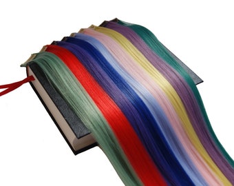 Könnte beinhalten: Ein Buch mit schwarzem Einband und einem roten Lesezeichen aus Band. Das Buch hat verschiedene farbige Haarverlängerungen, darunter rot, grün, blau, lila, gelb und rosa.