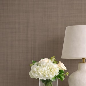 May include: A white bedside table with a lamp, flowers, and a bed. The lamp has a cream-colored shade and a speckled white base. A clear glass vase holds white flowers. The bed has a white headboard and bedding.