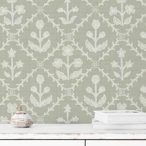 May include: Sage green wallpaper with a repeating white floral pattern. The design features stylized flowers and vines arranged in a diamond grid. A potted plant in a woven basket sits on a white surface.