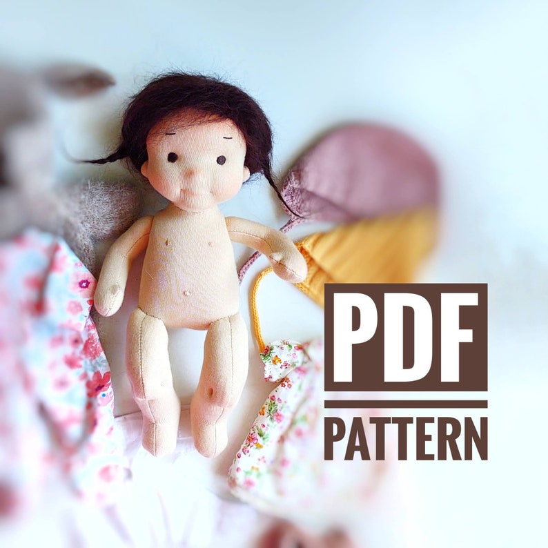 Puede incluir: Un patr&oacute;n PDF para una mu&ntilde;eca hecha a mano. La mu&ntilde;eca est&aacute; hecha de tela y tiene una tez marr&oacute;n claro, cabello negro y ojos marrones. La mu&ntilde;eca lleva un vestido blanco con estampado floral.