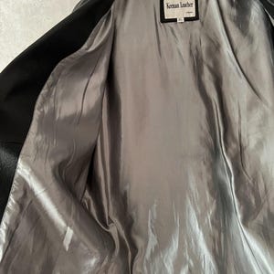 Peut inclure: Veste en cuir noir avec une doublure en satin gris. La veste est ouverte, r&eacute;v&eacute;lant la doublure int&eacute;rieure. Une &eacute;tiquette &agrave; l'int&eacute;rieur de la veste indique "Keenan Leather". La veste est suspendue &agrave; un cintre blanc.
