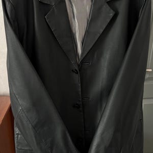 Peut inclure: Blazer en cuir noir avec col crant&eacute; et fermeture &agrave; trois boutons. La veste a un design classique avec une coupe ajust&eacute;e et des manches longues. L'&eacute;tiquette indique "Keenan Leather" et "XL".