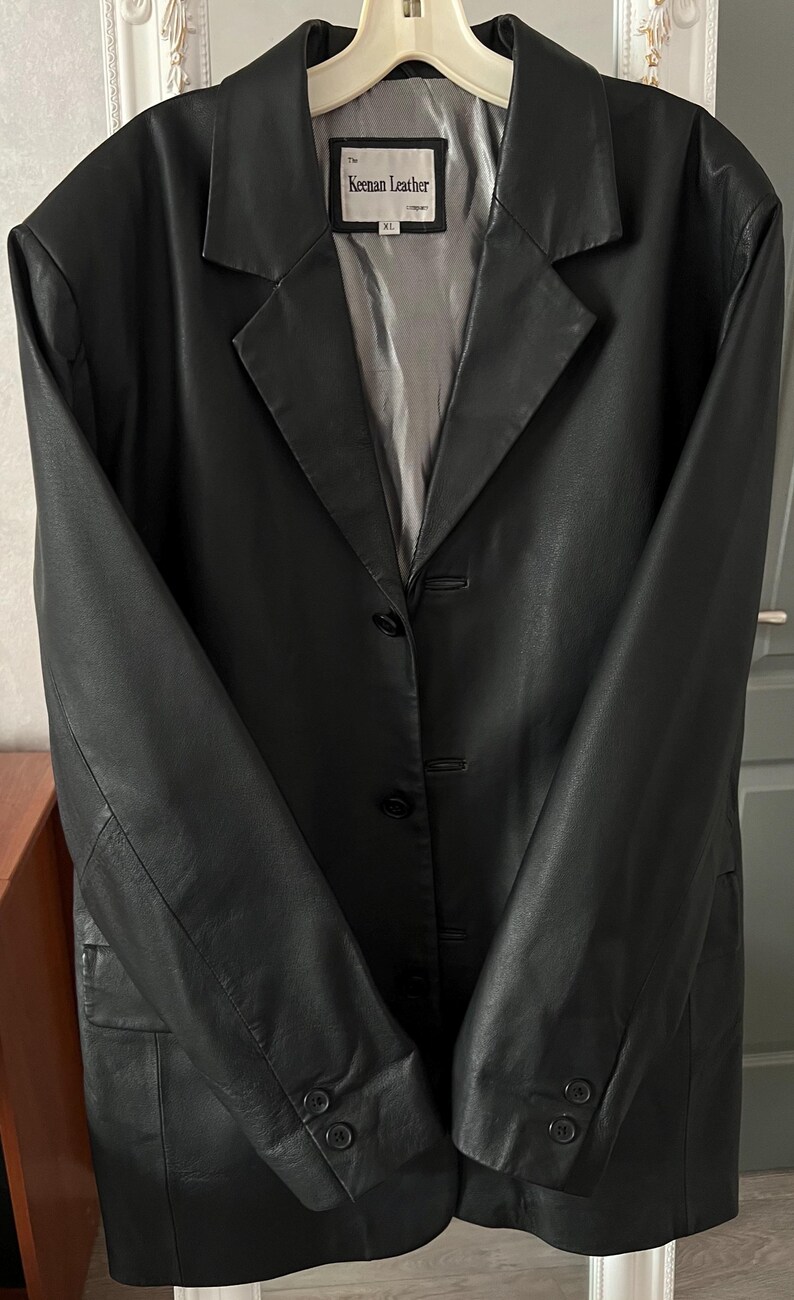 Peut inclure: Blazer en cuir noir avec col crant&eacute; et fermeture &agrave; trois boutons. La veste a un design classique avec une coupe ajust&eacute;e et des manches longues. L'&eacute;tiquette indique "Keenan Leather" et "XL".