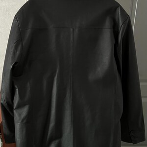 Peut inclure: Veste en cuir noir avec un col crant&eacute; et des poignets boutonn&eacute;s. Le dos de la veste pr&eacute;sente une fente centrale et des d&eacute;tails de couture verticaux. La veste est suspendue &agrave; un cintre.