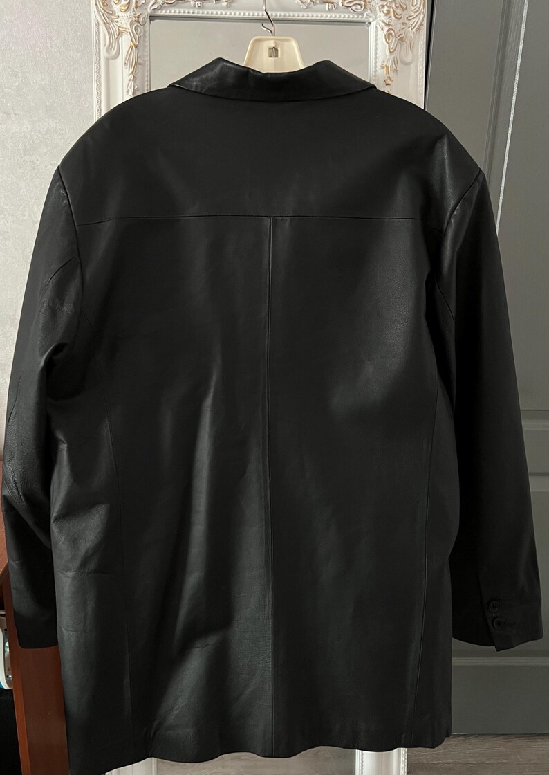 Peut inclure: Veste en cuir noir avec un col crant&eacute; et des poignets boutonn&eacute;s. Le dos de la veste pr&eacute;sente une fente centrale et des d&eacute;tails de couture verticaux. La veste est suspendue &agrave; un cintre.