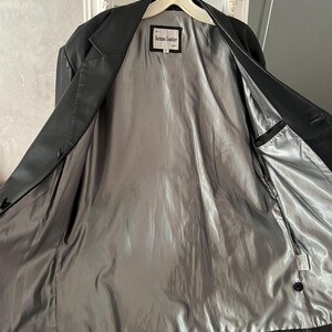 Peut inclure: Veste en cuir noir avec une doublure en satin gris. La veste est ouverte, r&eacute;v&eacute;lant la doublure int&eacute;rieure et une petite &eacute;tiquette qui indique "Keman Leather". La veste est suspendue &agrave; un cintre blanc.