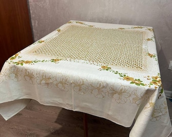 Könnte beinhalten: Eine weiße Tischdecke mit einem Blumenmuster mit gelben Blüten und grünen Blättern. Die Tischdecke hat ein gewebtes Design in der Mitte und einen Blumenrand an den Kanten.