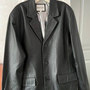 Peut inclure: Blazer en cuir noir avec revers crant&eacute;s, fermeture &agrave; trois boutons et deux poches avant. La veste a une doublure argent&eacute;e et l'&eacute;tiquette indique "Keenan Leather".