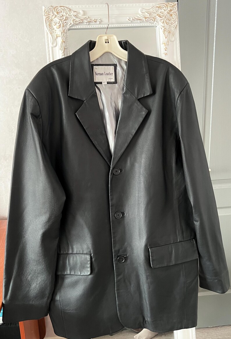 Peut inclure: Blazer en cuir noir avec revers crant&eacute;s, fermeture &agrave; trois boutons et deux poches avant. La veste a une doublure argent&eacute;e et l'&eacute;tiquette indique "Keenan Leather".