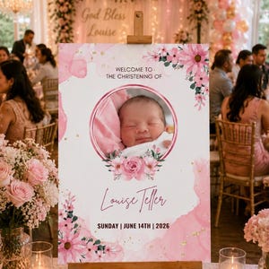 May include: A wooden easel displays a pink and white sign for a christening. The sign features a baby's photo, floral accents, and the text "Welcome to the Christening of Louise Teller, Sunday, June 14th, 2026."