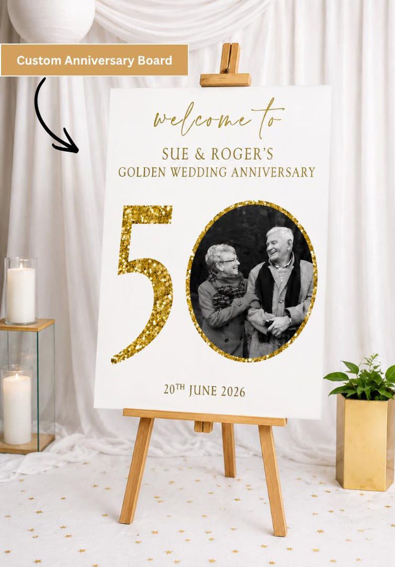 May include: A white custom anniversary board on a wooden easel. The board features gold text that reads "welcome to Sue & Roger's Golden Wedding Anniversary" and "50". A black and white photo is in the center.