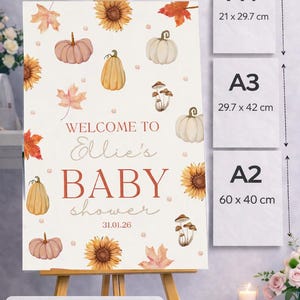 May include: A baby shower sign on an easel, featuring watercolor illustrations of pumpkins, sunflowers, and leaves. The sign reads "Welcome to Ellie's Baby Shower" with the date 31.01.26. Available sizes are A4 (8.3 x 11.7 inches), A3 (11.7 x 16.5 inches), and A2 (23.6 x 15.7 inches).