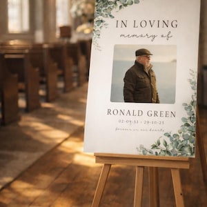 Peut inclure: Un chevalet en bois supportant un panneau comm&eacute;moratif. Le panneau affiche "IN LOVING memory of" au-dessus d'une photo d'un homme. Le nom "RONALD GREEN" et des dates sont en dessous. Le panneau est orn&eacute; de verdure.