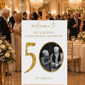 May include: A white sign on a wooden easel with gold text that reads "welcome to SUE & ROGER'S GOLDEN WEDDING ANNIVERSARY". A gold glitter "50" and a black and white photo of a couple are featured. The date "20th JUNE 2026" is also displayed.