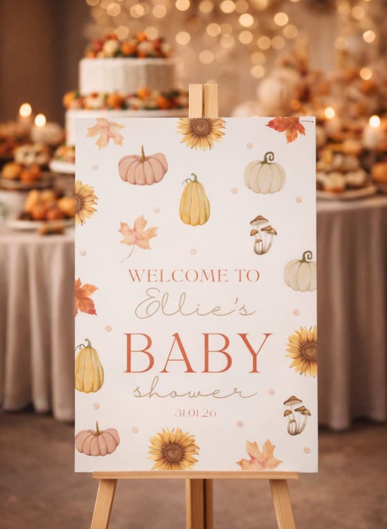 May include: A wooden easel displays a baby shower welcome sign. The sign features watercolor illustrations of pumpkins, sunflowers, and leaves. Text reads "Welcome to Ellie's Baby Shower" with the date 31.01.26.