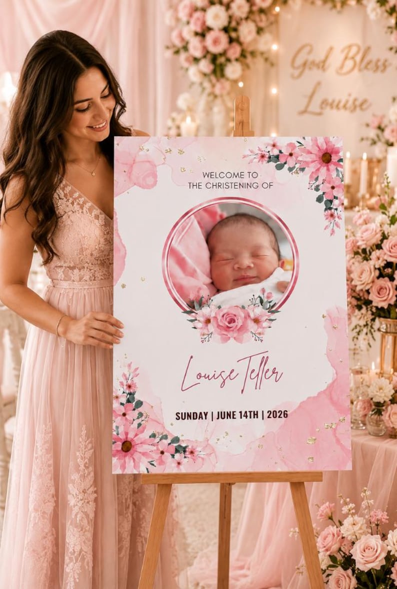 May include: A pink and white christening sign on an easel. The sign features a baby's photo surrounded by flowers, with the text "Welcome to the Christening of Louise Teller, Sunday | June 14th | 2026." The background includes floral arrangements.