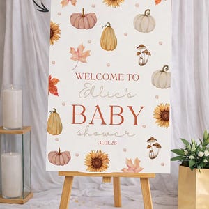 May include: A baby shower sign on a wooden easel. The sign features watercolor illustrations of pumpkins, sunflowers, and leaves. Text reads "Welcome to Ellie's BABY shower 31.01.26". The sign is decorated with fall-themed elements.