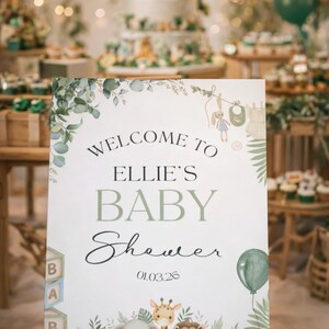Pu&ograve; includere: Un cartello di benvenuto per il baby shower di Ellie, con uno sfondo bianco ornato da foglie verdi e illustrazioni di animali. Il cartello recita "Benvenuti al baby shower di Ellie" e la data 01.03.26.