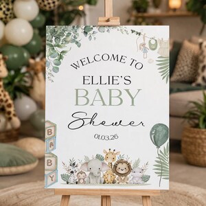 Pu&ograve; includere: Un cavalletto di legno espone un cartello per il baby shower con la scritta "Welcome to Ellie's Baby Shower 01.03.26." Il cartello presenta un design floreale verde e bianco e illustrazioni di animali per bambini. &Egrave; raffigurato anche un palloncino verde.