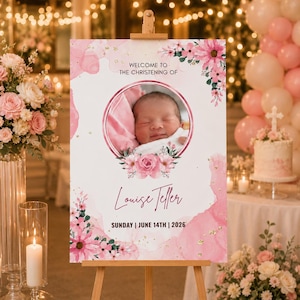 May include: A pink and gold christening welcome sign on an easel. The sign displays a baby's photo in a floral frame, the name "Louise Teller", and the date "Sunday | June 14th | 2026".