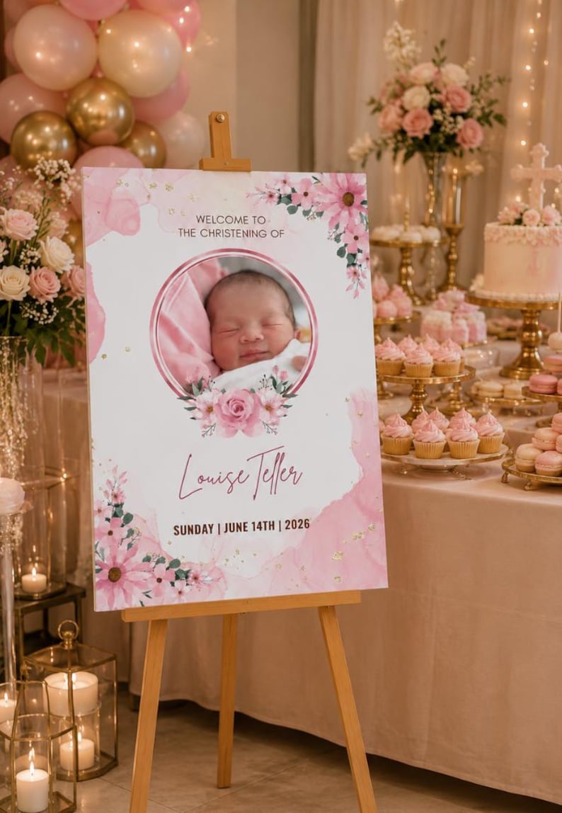 May include: A christening welcome sign with a baby's photo in a pink floral frame. The sign displays the name "Louise Teller" and the date "June 14th, 2026". The sign is on a wooden easel, with pink and gold balloons and floral arrangements in the background.
