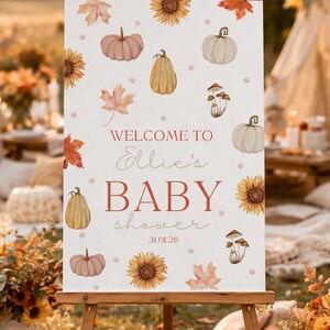 May include: A wooden easel displays a sign with a baby shower theme. The sign features watercolor illustrations of pumpkins, sunflowers, and leaves. Text reads "Welcome to Ellie's BABY shower 31.01.26."