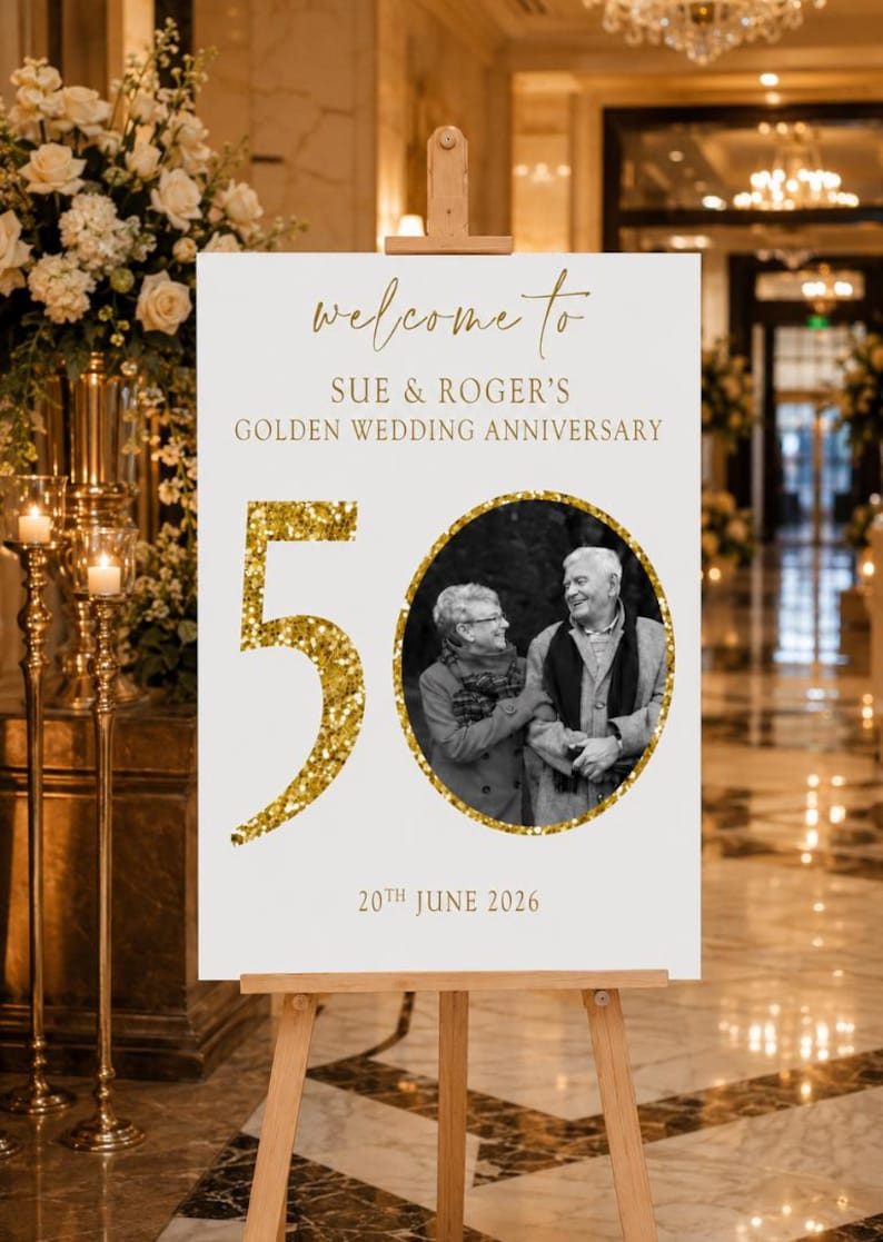 May include: A white sign on a wooden easel with gold text that reads "Welcome to Sue & Roger's Golden Wedding Anniversary." A photo of a couple is in a gold circle, with a large gold glitter "50" and the date "20th June 2026".