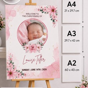 May include: A pink and white christening sign on an easel, with a baby's photo and floral design. The sign reads "Welcome to the Christening of Louise Teller, Sunday, June 14th, 2026." Available sizes are A4 (21 x 29.7 cm), A3 (29.7 x 42 cm), and A2 (60 x 40 cm).