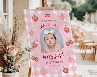 May include: A rectangular birthday sign featuring a pink and white gingham pattern, a central photo of a child, and the text: WELCOME TO MATILDA'S berry first BIRTHDAY 28TH AUGUST 2026. The design includes illustrations of strawberries with pink bows.