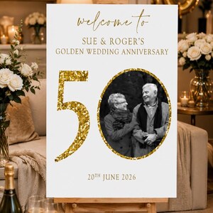 May include: A white sign on an easel with gold text that reads "welcome to SUE & ROGER'S GOLDEN WEDDING ANNIVERSARY." A black and white photo of a couple is in a gold circle. The number "50" is in gold glitter.