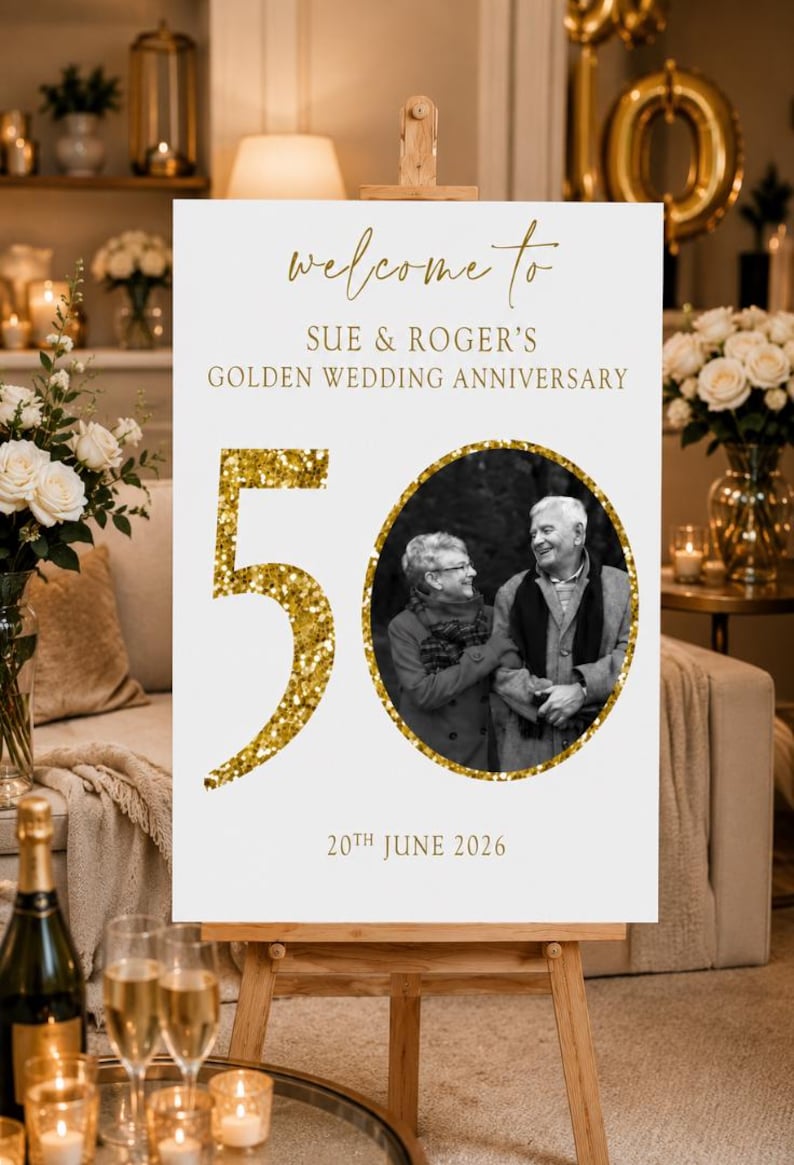 May include: A white sign on an easel with gold text that reads "welcome to SUE & ROGER'S GOLDEN WEDDING ANNIVERSARY." A black and white photo of a couple is in a gold circle. The number "50" is in gold glitter.
