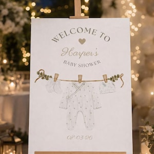 May include: A wooden easel displays a baby shower sign. The sign reads "Welcome to Harper's Baby Shower" with a heart graphic. A clothesline illustration features baby clothes, including a onesie, mittens, and a hat. The date "08-03-26" is printed at the bottom.