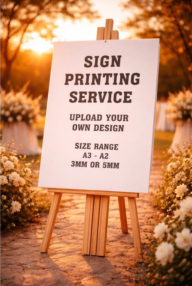 May include: A white sign on a wooden easel, displaying "SIGN PRINTING SERVICE" and "UPLOAD YOUR OWN DESIGN." The size range is A3-A2, with options for 3mm or 5mm thickness. The background features flowers and a warm, golden light.