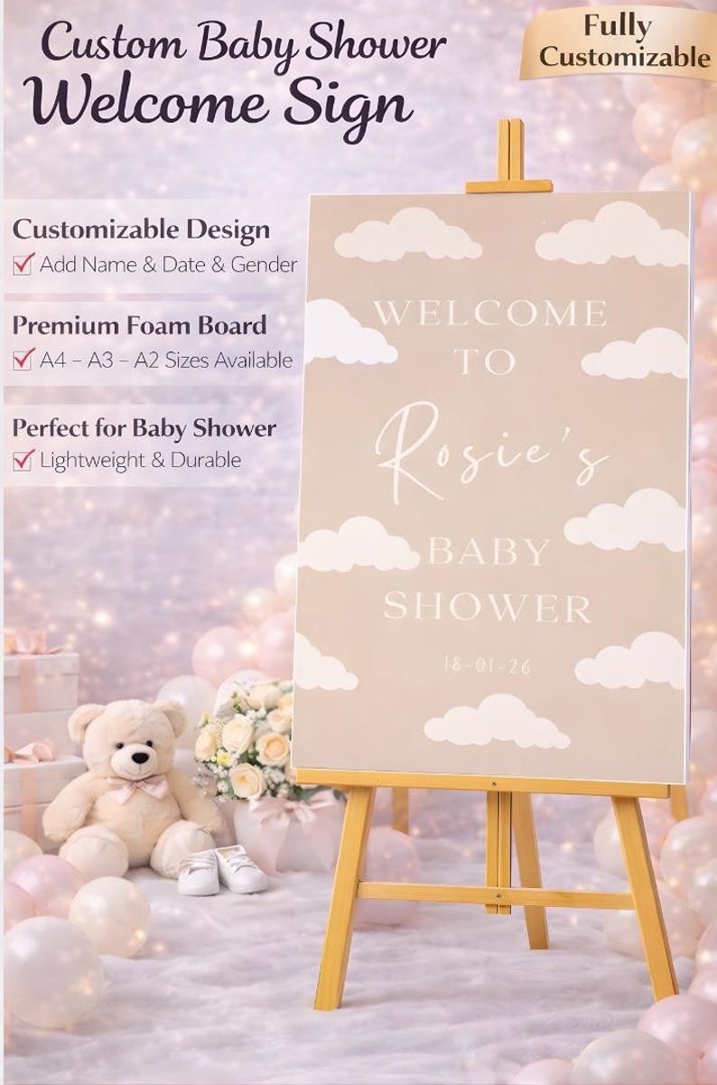 Op de afbeelding: Een gepersonaliseerd welkomstbord voor een babyshower op een houten ezel. Het beige bord heeft witte wolkenaccenten en de tekst "Welcome to Rosie's Baby Shower" met de datum. Volledig aanpasbaar.