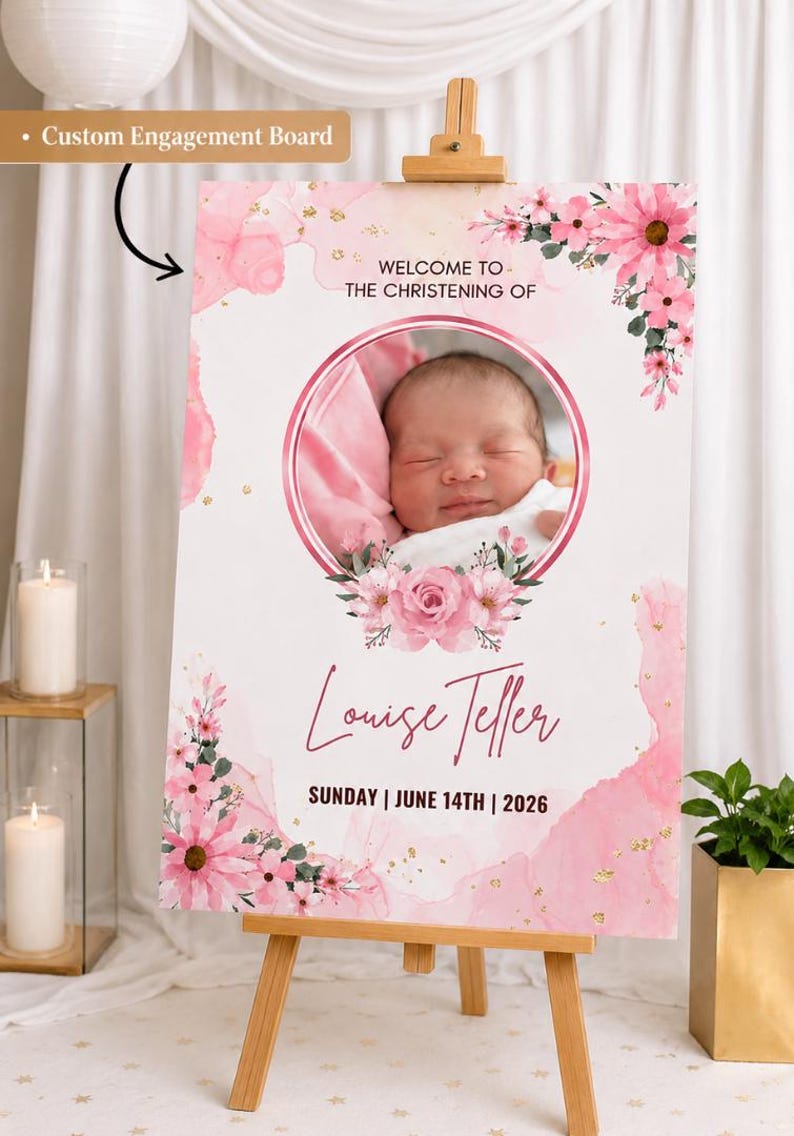 May include: A christening sign on a wooden easel, featuring a baby's photo within a pink floral frame. The sign reads "Welcome to the Christening of Louise Teller" and the date "Sunday | June 14th | 2026".