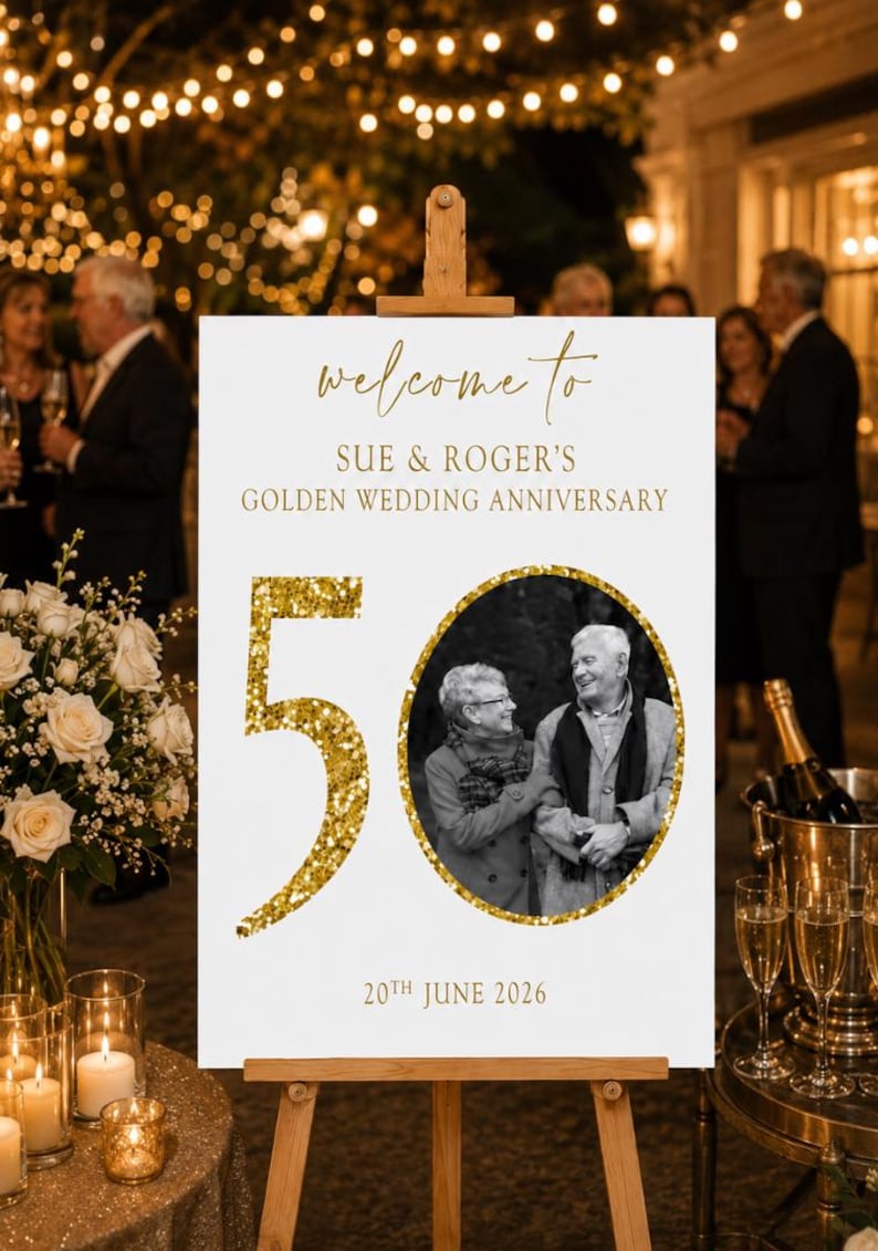 May include: A white sign on a wooden easel with gold text that reads "welcome to SUE & ROGER'S GOLDEN WEDDING ANNIVERSARY". A gold glitter "50" and a black and white photo of a couple are also on the sign. The date "20th JUNE 2026" is at the bottom.