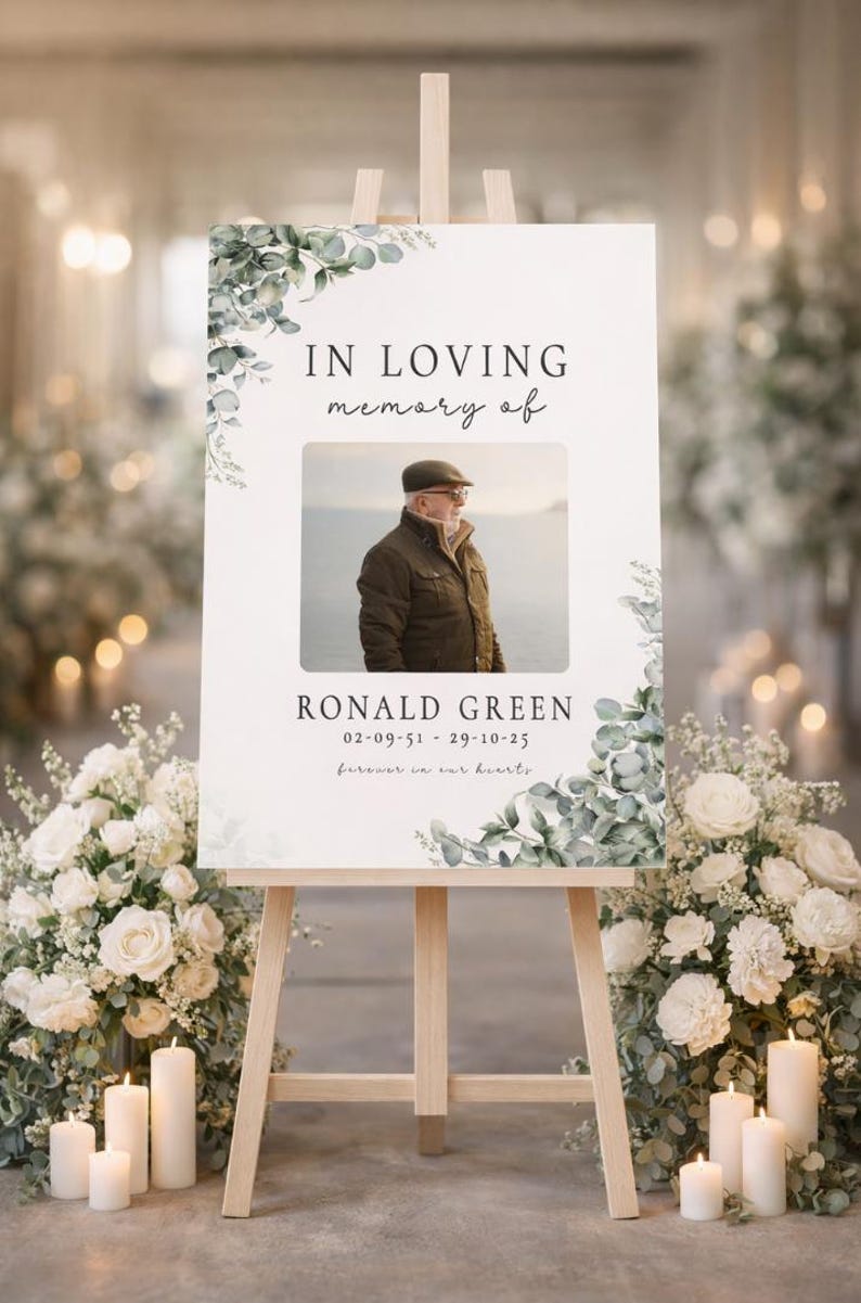 Peut inclure: Un panneau comm&eacute;moratif sur un chevalet en bois, avec le texte "IN LOVING memory of" au-dessus d'une photo d'un homme. Le panneau comprend le nom "RONALD GREEN" et des dates, avec des motifs floraux. Des fleurs blanches et des bougies entourent le chevalet.