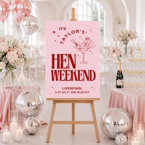 May include: A pink sign on a wooden easel with the text "IT'S TAYLOR'S, HEN WEEKEND, LIVERPOOL 31ST JULY- 2ND AUGUST". The sign has a graphic of a woman in a martini glass. The scene includes disco balls, flowers, and champagne.