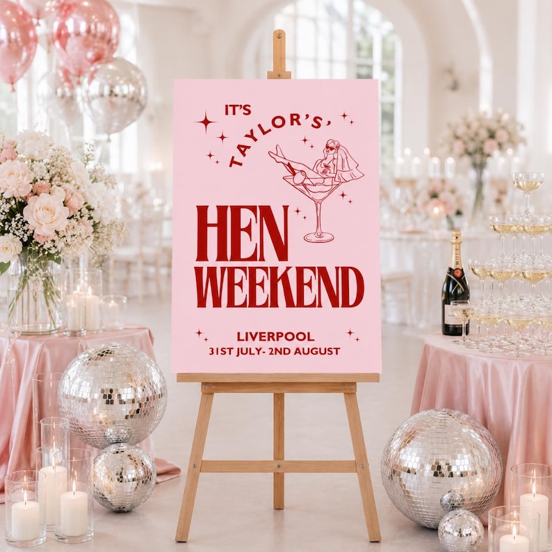 May include: A pink sign on a wooden easel with the text "IT'S TAYLOR'S, HEN WEEKEND, LIVERPOOL 31ST JULY- 2ND AUGUST". The sign has a graphic of a woman in a martini glass. The scene includes disco balls, flowers, and champagne.